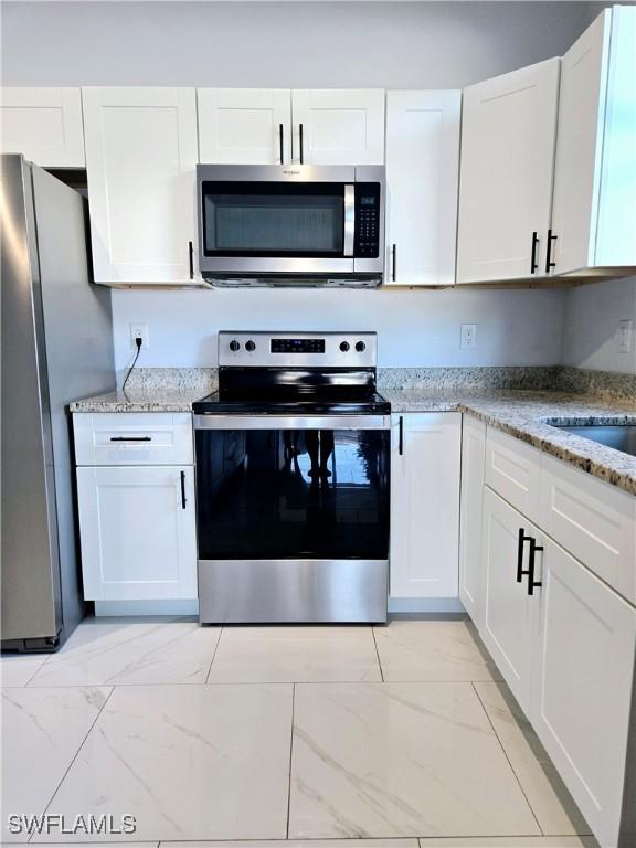 kitchen with light stone counters, sink, white cabinets, and stainless steel appliances