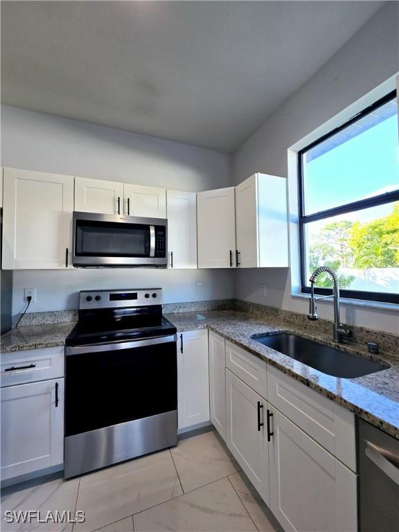 kitchen featuring white cabinetry, sink, light stone counters, and appliances with stainless steel finishes