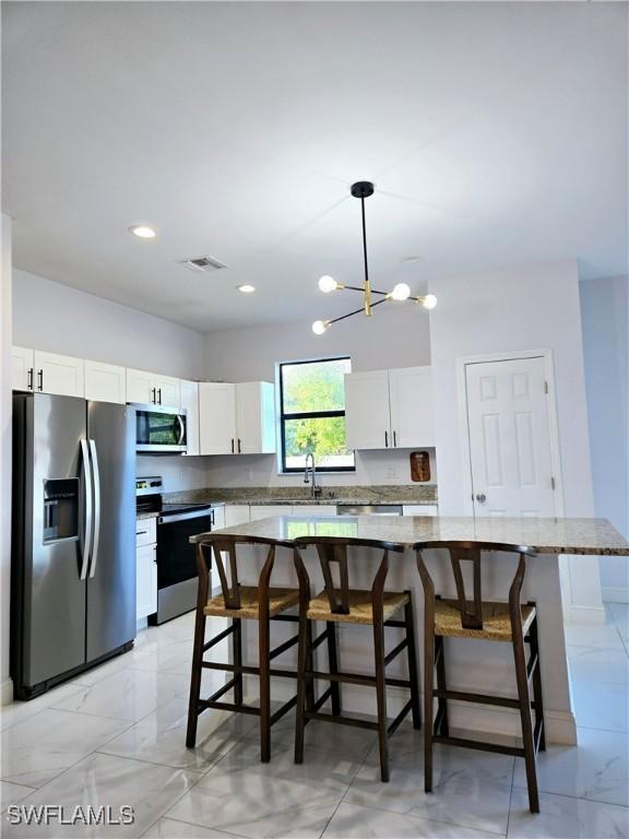 kitchen featuring marble finish floor, pendant lighting, stainless steel appliances, white cabinets, and a sink