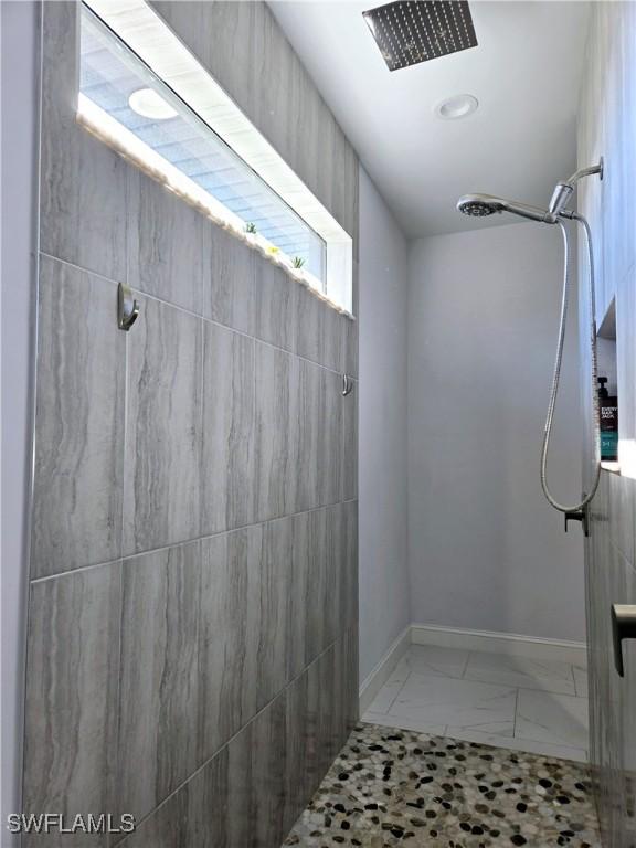 bathroom with marble finish floor, tiled shower, and baseboards