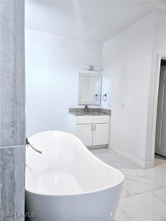 bathroom with marble finish floor, vanity, baseboards, and a soaking tub