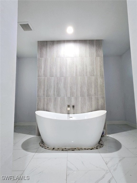 full bath featuring marble finish floor, a freestanding tub, visible vents, and tile walls