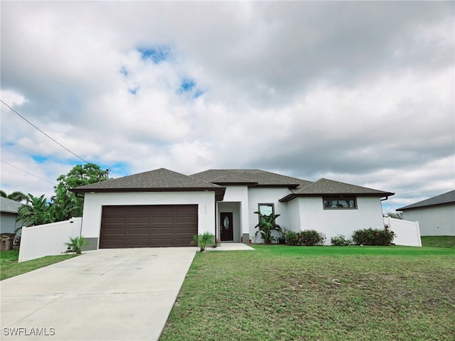 prairie-style home with a garage, fence, concrete driveway, stucco siding, and a front yard