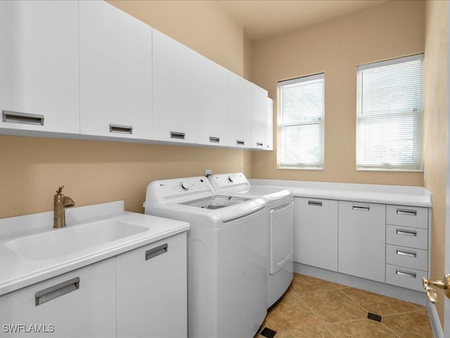 clothes washing area with washer and clothes dryer, sink, light tile patterned floors, and cabinets