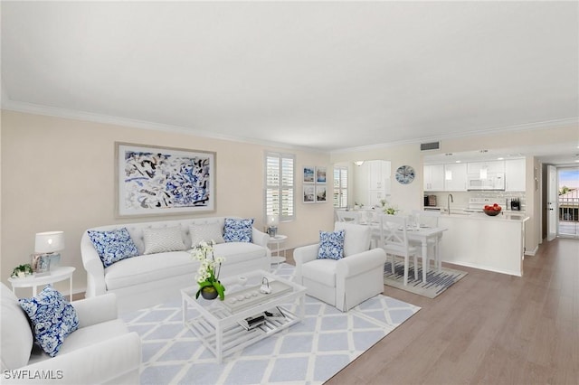 living room with light hardwood / wood-style floors, sink, and crown molding