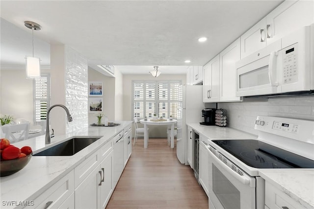 kitchen featuring light wood-type flooring, white appliances, sink, pendant lighting, and white cabinets