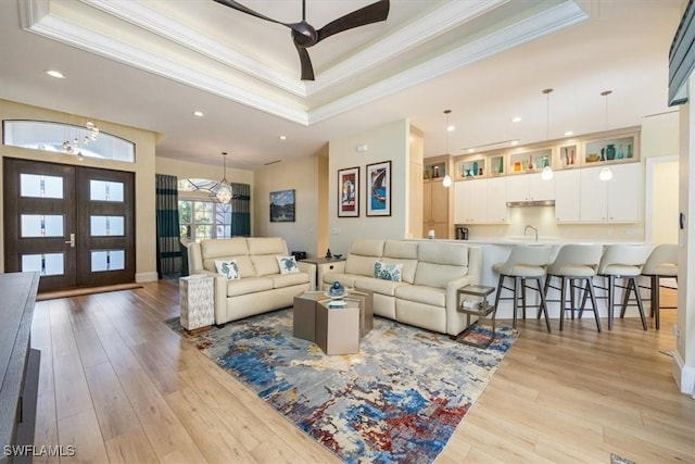 living room with ceiling fan with notable chandelier, crown molding, a tray ceiling, and light hardwood / wood-style flooring