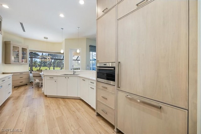 kitchen with light wood-type flooring, sink, oven, hanging light fixtures, and built in fridge