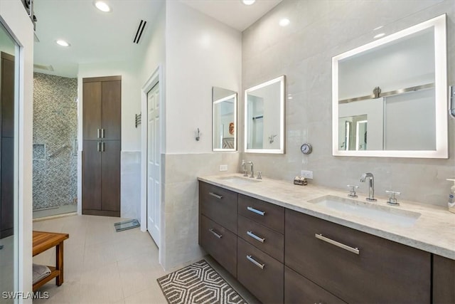 bathroom featuring a tile shower, tile patterned flooring, vanity, and tile walls