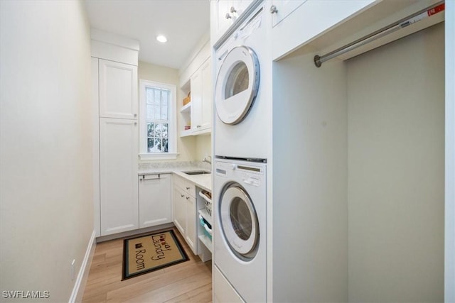 laundry area featuring stacked washing maching and dryer, sink, cabinets, and light wood-type flooring