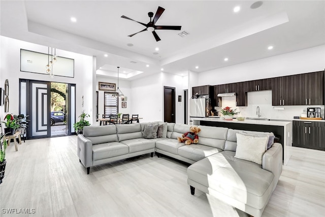 living room with ceiling fan, sink, light hardwood / wood-style flooring, and a tray ceiling