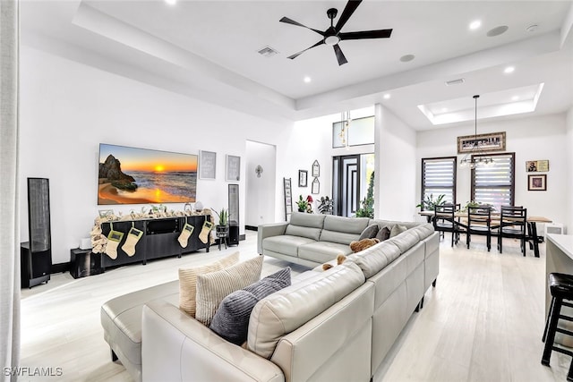 living room featuring a raised ceiling, a towering ceiling, light hardwood / wood-style flooring, and ceiling fan