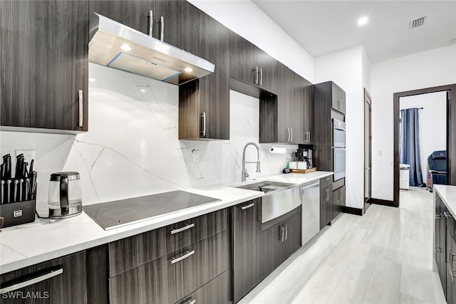 kitchen with sink, tasteful backsplash, dark brown cabinets, appliances with stainless steel finishes, and light wood-type flooring