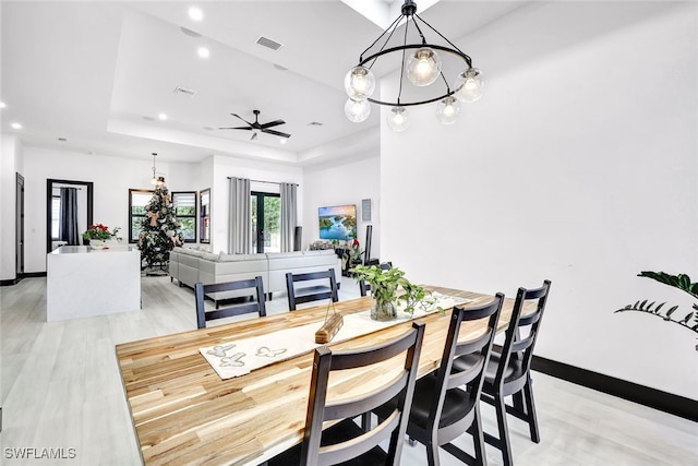 dining space featuring a tray ceiling, ceiling fan with notable chandelier, and light wood-type flooring