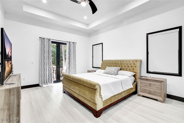 bedroom with access to exterior, ceiling fan, french doors, light hardwood / wood-style flooring, and a tray ceiling