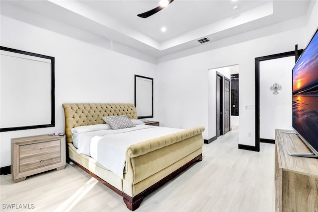 bedroom featuring ceiling fan, a raised ceiling, and light hardwood / wood-style flooring