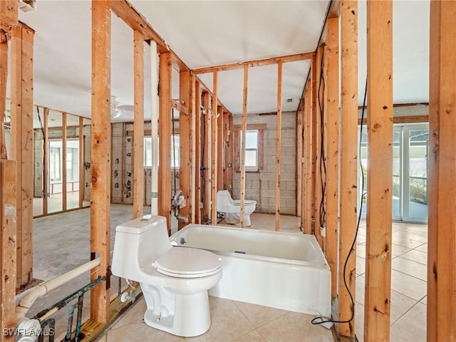 bathroom featuring a wealth of natural light, a washtub, tile patterned flooring, and toilet