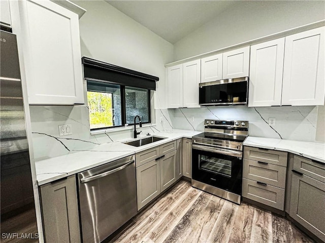 kitchen with white cabinetry, sink, light hardwood / wood-style flooring, lofted ceiling, and appliances with stainless steel finishes