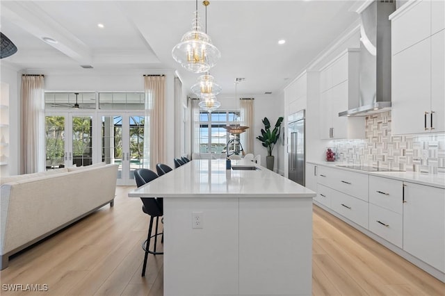 kitchen featuring pendant lighting, light hardwood / wood-style floors, a kitchen island with sink, and wall chimney range hood