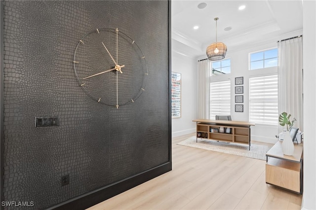 hallway featuring a raised ceiling, light wood-type flooring, and crown molding