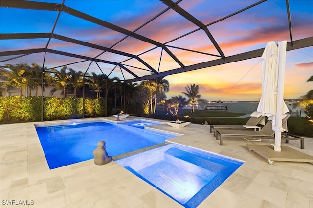 pool at dusk featuring a lanai, a patio area, and an in ground hot tub