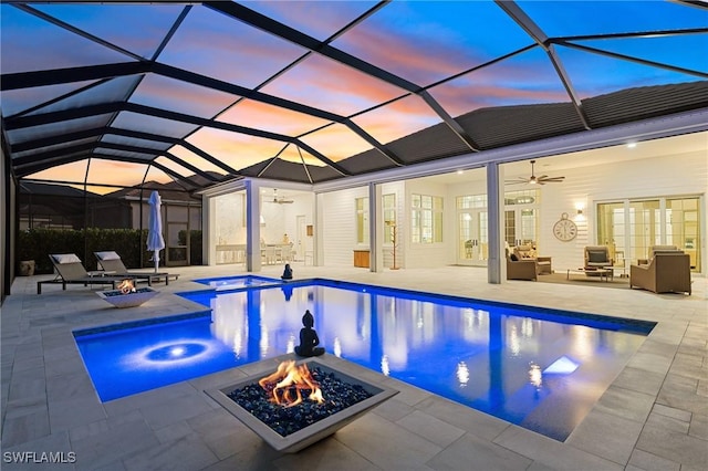 pool at dusk with ceiling fan, a lanai, an outdoor living space with a fire pit, an in ground hot tub, and a patio