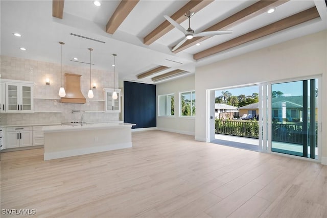 kitchen with custom exhaust hood, decorative light fixtures, light hardwood / wood-style flooring, a center island with sink, and white cabinets