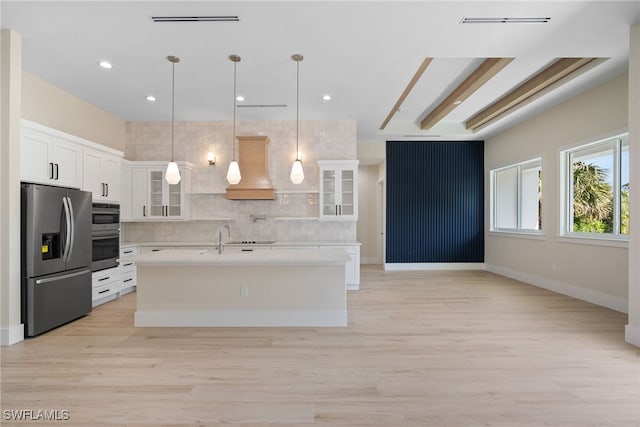 kitchen with custom range hood, stainless steel appliances, pendant lighting, white cabinets, and light hardwood / wood-style floors