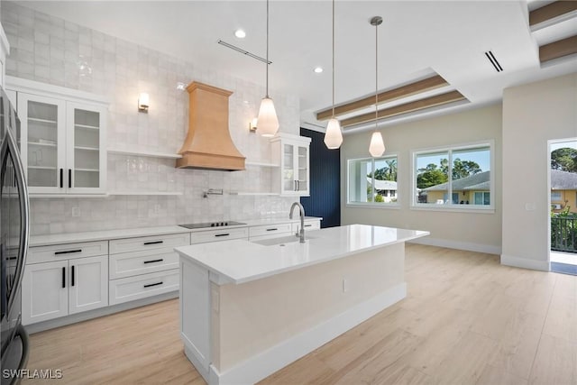 kitchen with sink, backsplash, white cabinets, custom range hood, and light wood-type flooring