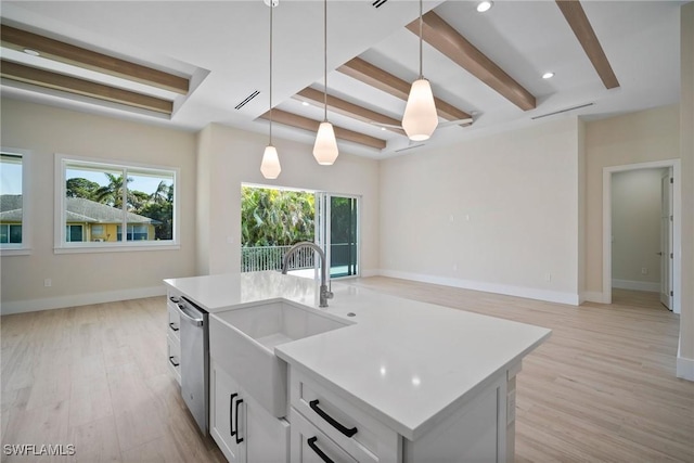 kitchen featuring stainless steel dishwasher, light hardwood / wood-style floors, decorative light fixtures, a center island with sink, and white cabinets