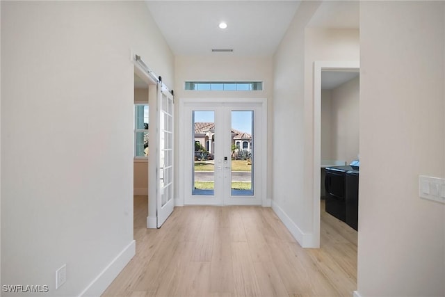 interior space with a barn door, french doors, and light wood-type flooring