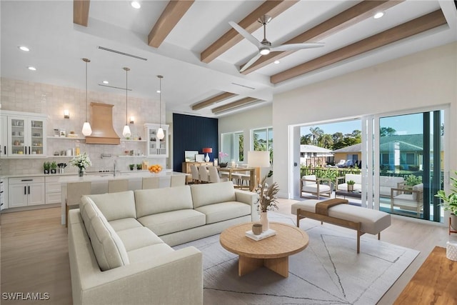 living room with beam ceiling, ceiling fan, a healthy amount of sunlight, and light wood-type flooring