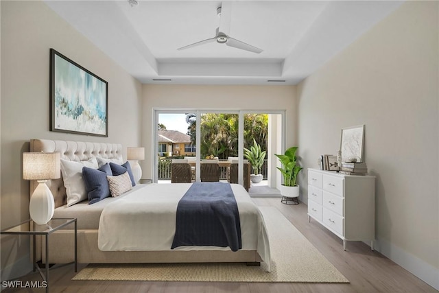 bedroom with a tray ceiling, access to exterior, ceiling fan, and light hardwood / wood-style floors