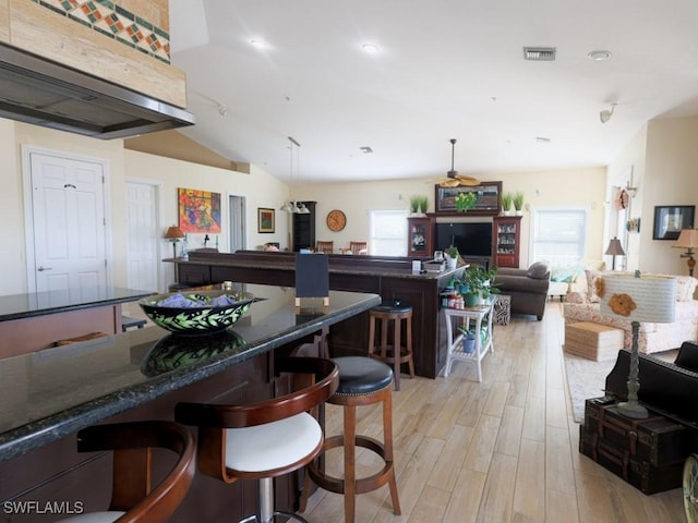 kitchen featuring a kitchen breakfast bar, light wood-type flooring, decorative light fixtures, and vaulted ceiling