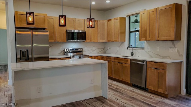 kitchen featuring sink, stainless steel appliances, decorative light fixtures, and light hardwood / wood-style floors