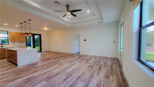 kitchen featuring ceiling fan, light stone countertops, light wood-type flooring, a tray ceiling, and decorative light fixtures