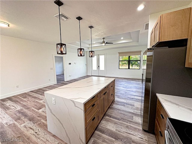 kitchen with ceiling fan, a kitchen island, dark hardwood / wood-style flooring, and a tray ceiling