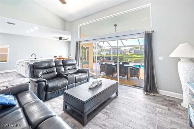 living room featuring ceiling fan, sink, high vaulted ceiling, and light hardwood / wood-style floors