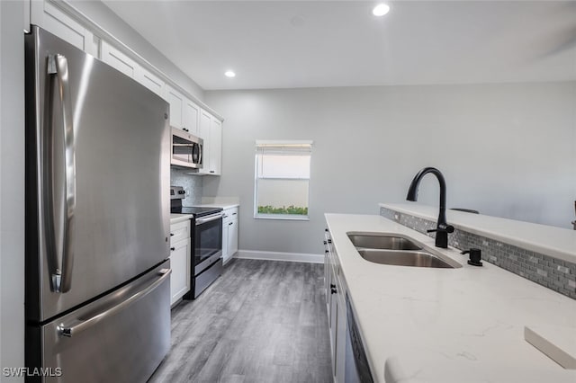 kitchen with white cabinets, sink, appliances with stainless steel finishes, light stone counters, and wood-type flooring