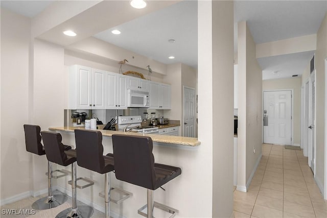 kitchen with a kitchen bar, kitchen peninsula, white appliances, white cabinetry, and light tile patterned flooring