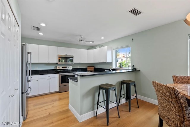 kitchen with white cabinets, light hardwood / wood-style floors, kitchen peninsula, and appliances with stainless steel finishes