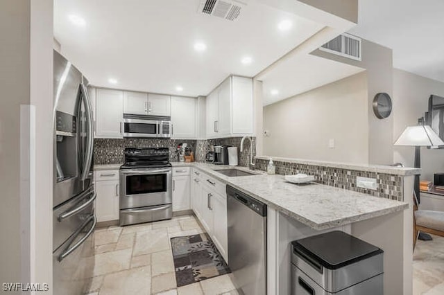 kitchen with sink, kitchen peninsula, light stone countertops, white cabinetry, and stainless steel appliances