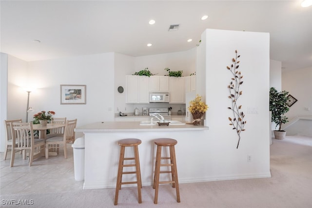 kitchen with kitchen peninsula, white appliances, white cabinets, and light colored carpet