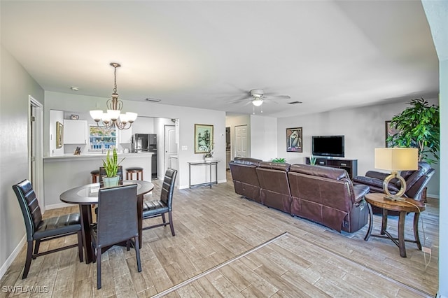 dining space with ceiling fan with notable chandelier and light hardwood / wood-style floors