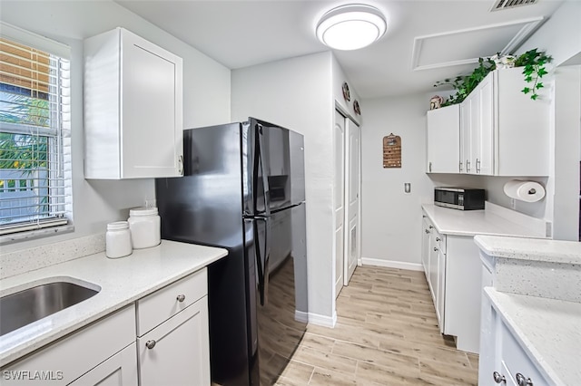 kitchen with white cabinetry, light stone countertops, sink, black fridge, and light hardwood / wood-style flooring