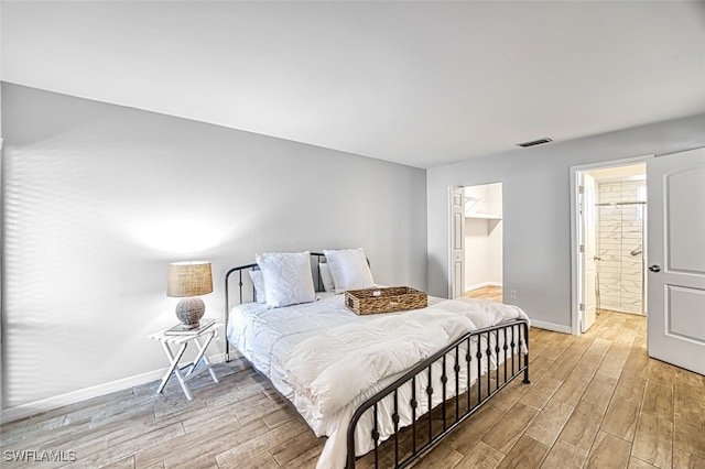 bedroom with ensuite bathroom, light hardwood / wood-style floors, and a walk in closet