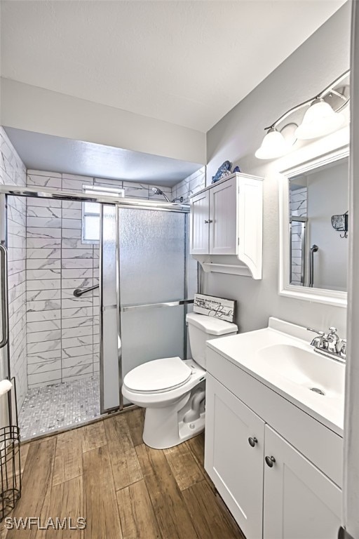 bathroom with hardwood / wood-style floors, vanity, an enclosed shower, and toilet