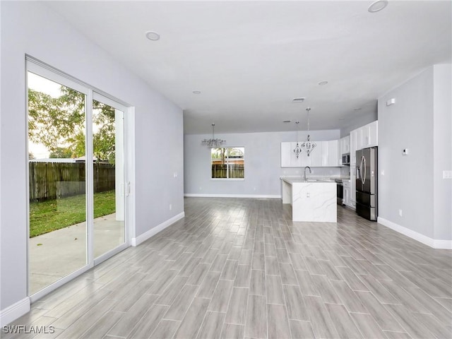 unfurnished living room featuring light wood-type flooring, an inviting chandelier, and a wealth of natural light