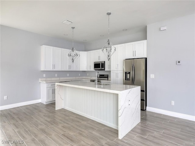 kitchen with appliances with stainless steel finishes, a center island with sink, light hardwood / wood-style flooring, white cabinetry, and hanging light fixtures