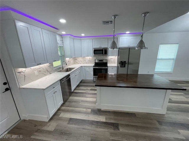 kitchen featuring sink, hanging light fixtures, white cabinets, a kitchen island, and appliances with stainless steel finishes